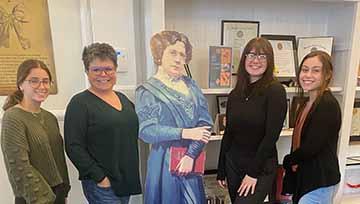 Four women stand together with a cutout of a historic women between them