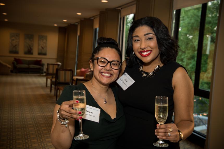 Two young alumnae pose for the camera with champagne glasses