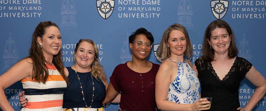 Five women pose in front of NDMU backdrop