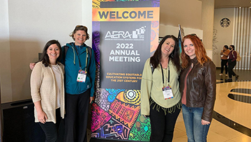 Four NDMU students and faculty pose in front of a welcome sign at the AERA conference