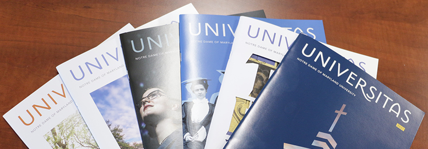 Six editions of Universitas fanned out on a brown tabletop