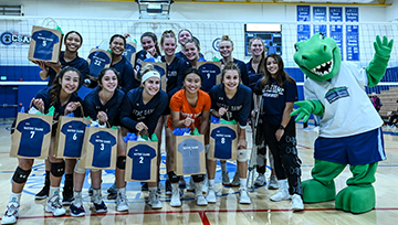 Volleyball team poses in front of net with Gabby the Gator