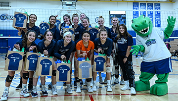 Volleyball team poses in front of net with Gabby the Gator