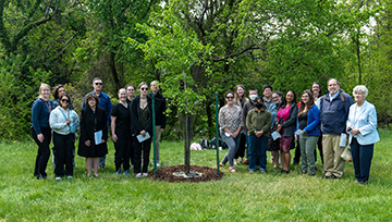 NDMU communities member in front of a tree newly dedicated for Dr. Weldon