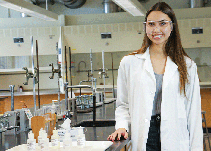 student wearing protective glasses and a lab coat in the lab