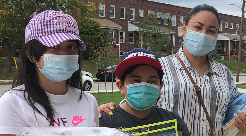 Woman with two kids wearing masks and holding school supplies