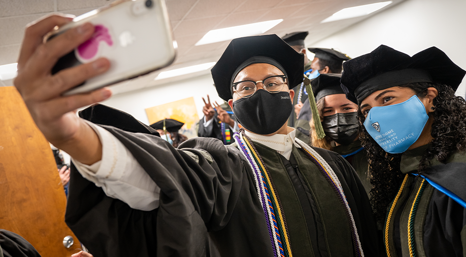 Masked pharmacy grads taking a selfie in graduation garb