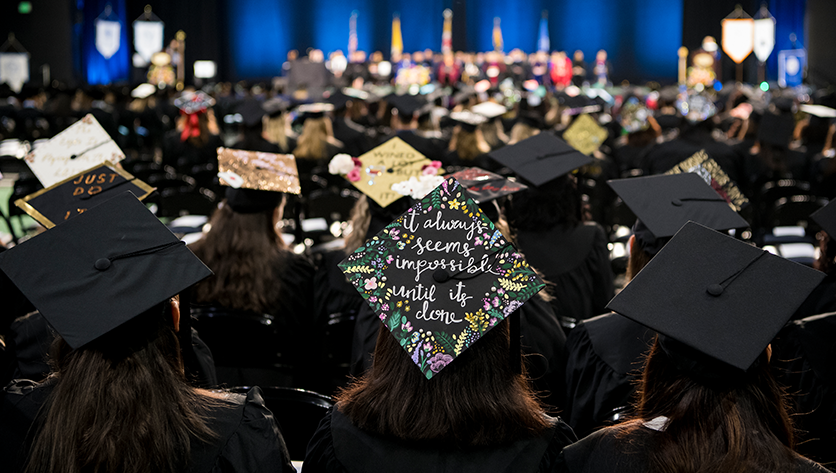 Back of a crowd of seated graduates with grad caps at commencement