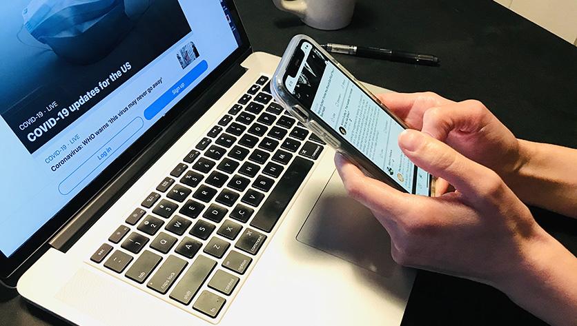 person reading news story on phones in front of their laptop