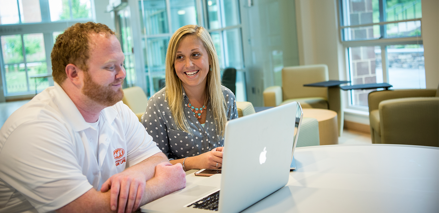 Male and female student smile in front of a laptop