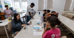 Female student wearing NDMU shirt smiles as she sits at a table across from a child