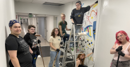 Female students pose while working on the STEAM mural