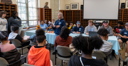 Female student stands in front of a group of seated children