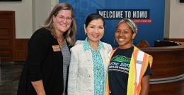 Cathy Goucher, Yumi Hogan, and Aniyah Plumer stand in front of a Welcome to NDMU backdrop
