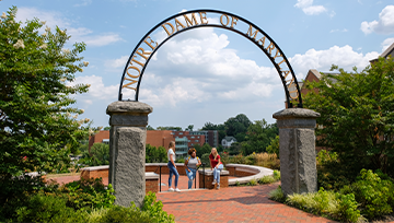 3 students sitting under the NDMU Arch
