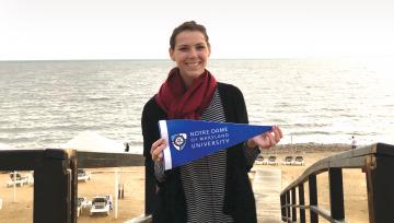 student holding NDMU flag near sea