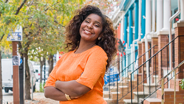 Woman smiling on a tree-lined street, in front of brick row houses