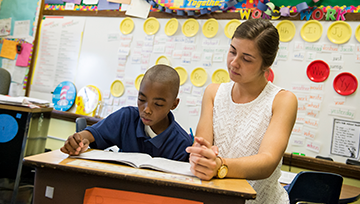 Teacher kneeling next to a student's desk looking at a book