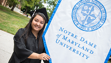 Student in cap and gown holding an NDMU banner