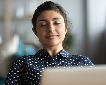 woman with her eyes closed breathing deeply in front of her laptop