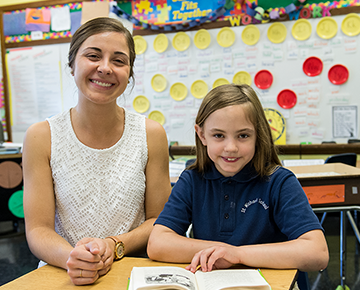 Smiling teacher and student sitting at a desk in a classroom