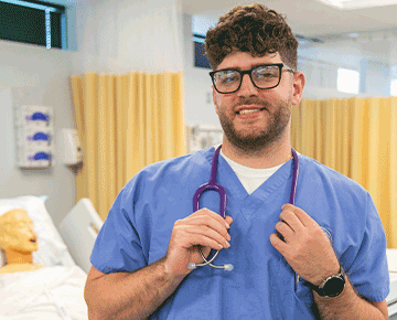 Male nurse holding a stethoscope around his neck in the sim lab