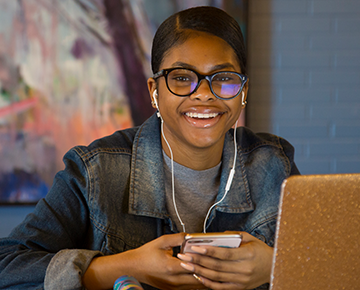 Smiling student wearing headphones, holding a phone and with a laptop