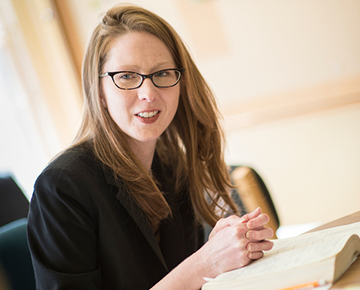 Faculty member wearing glasses sitting with a textbook