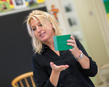 Female teacher holding a green cube in a classroom