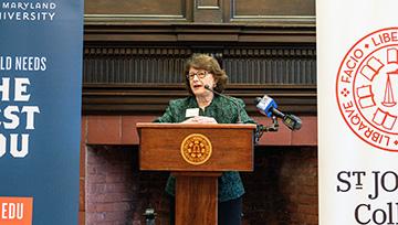 President Yam stands at a podium with NDMU and SJC banners on either side