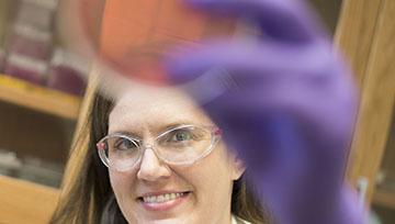 Jenifer Kerr holds up petri dish while wearing goggles