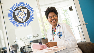 Nursing student reading a book in front of the School of Nursing logo