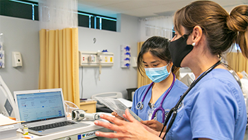 Nurses wearing masks having a discussion next to a laptop