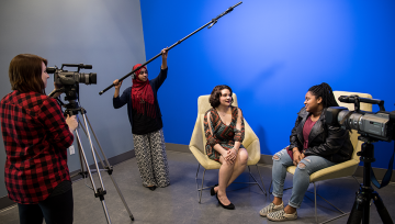 Students in front of the blue screen using the video and audio equipment to record an interview