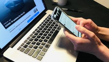 hands hold cell phone in front of laptop