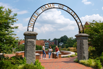 3 students sitting under the NDMU Arch