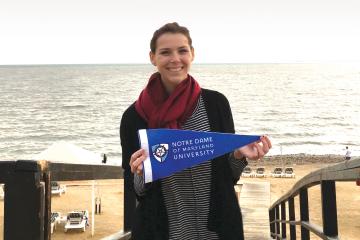 student holding NDMU flag near sea