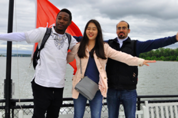 3 ELI students posing in front of water with arms open wide