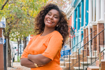 Woman smiling on a tree-lined street, in front of brick row houses