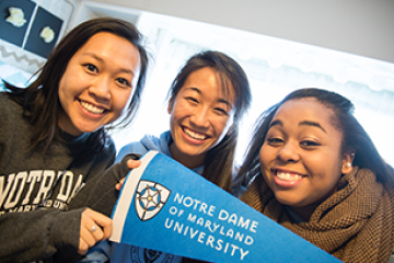 Three female students holding an NDMU pennant