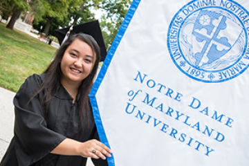 Student in cap and gown holding an NDMU banner