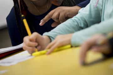 Hands of teacher and student working with pencil and paper