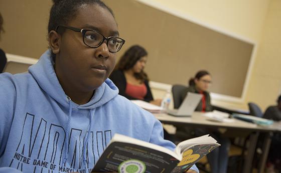 Woman wearing light blue NDMU hoodie sits in a classroom