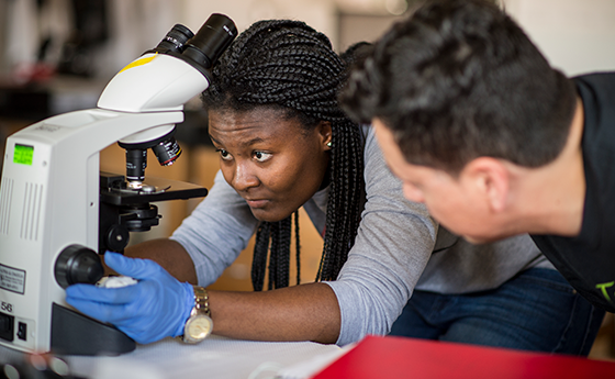 Student looking through microscope with a teacher