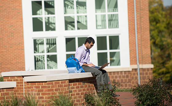 Grad student on a laptop outside sitting on a ledge