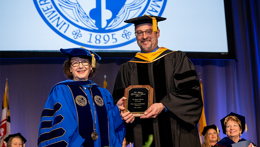 James Culhane wearing regalia holds a plaque as he stands with President Yam