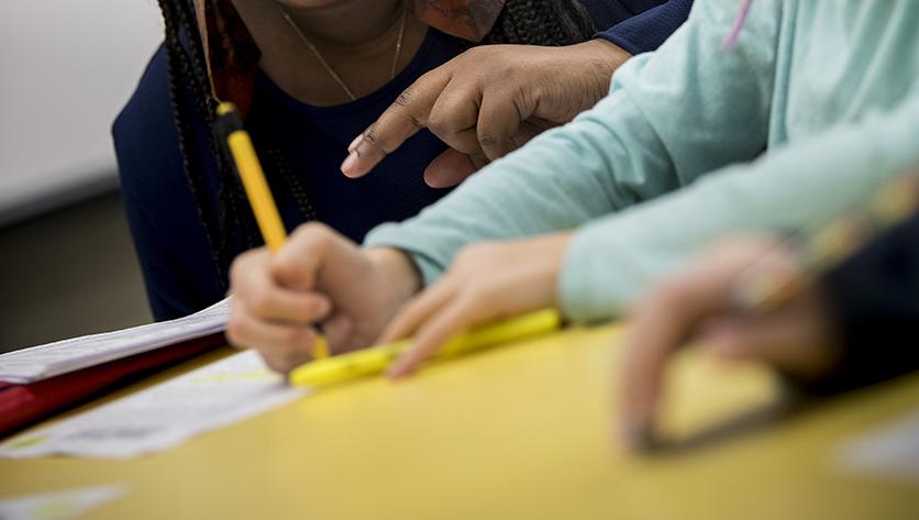 Hands of teacher and student working with pencil and paper