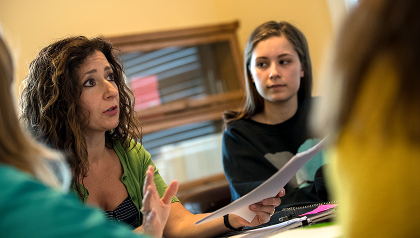 teacher speaks to group of students at table`