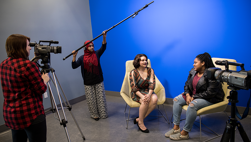 Students in front of the blue screen using the video and audio equipment to record an interview