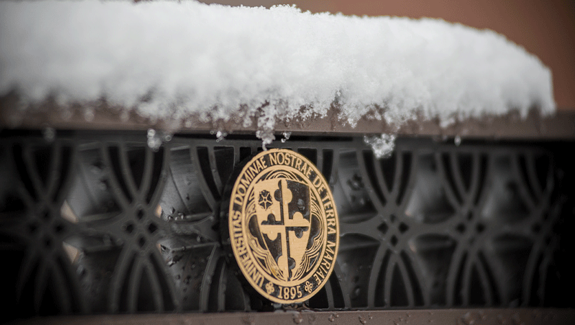 snow on top of a sign with the NDMU seal
